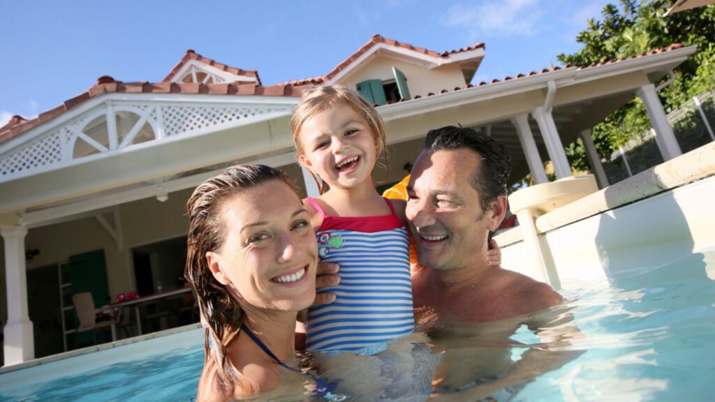 Family playing in swimming pool of private villa. Travel Concept.