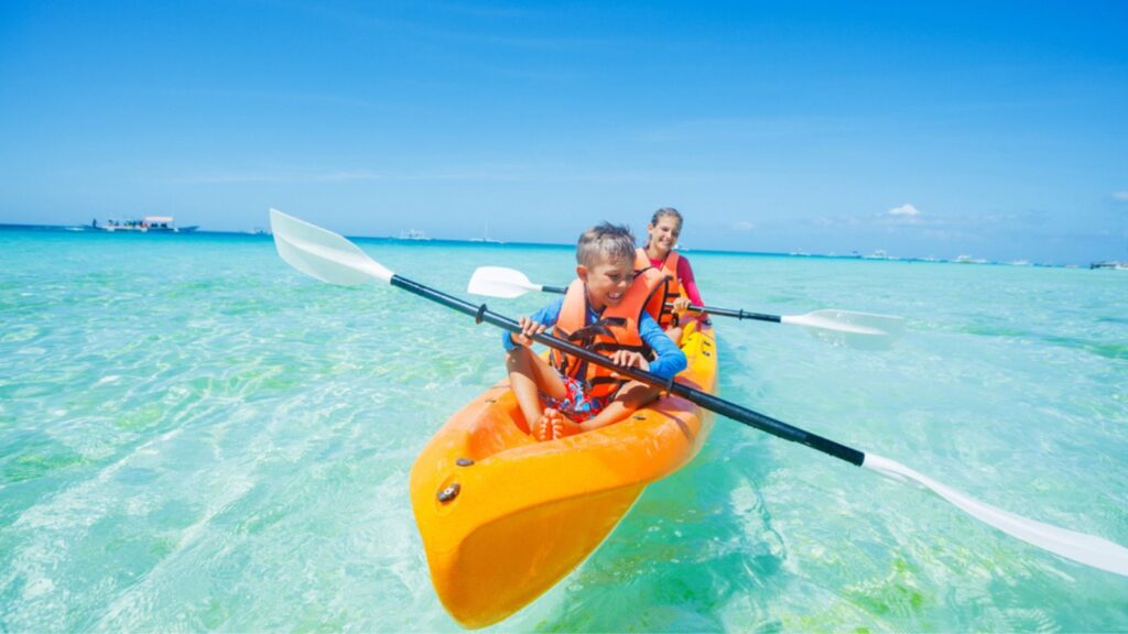 Happy boy and girl kayaking at tropical sea on yellow kayak. Travel Concept.