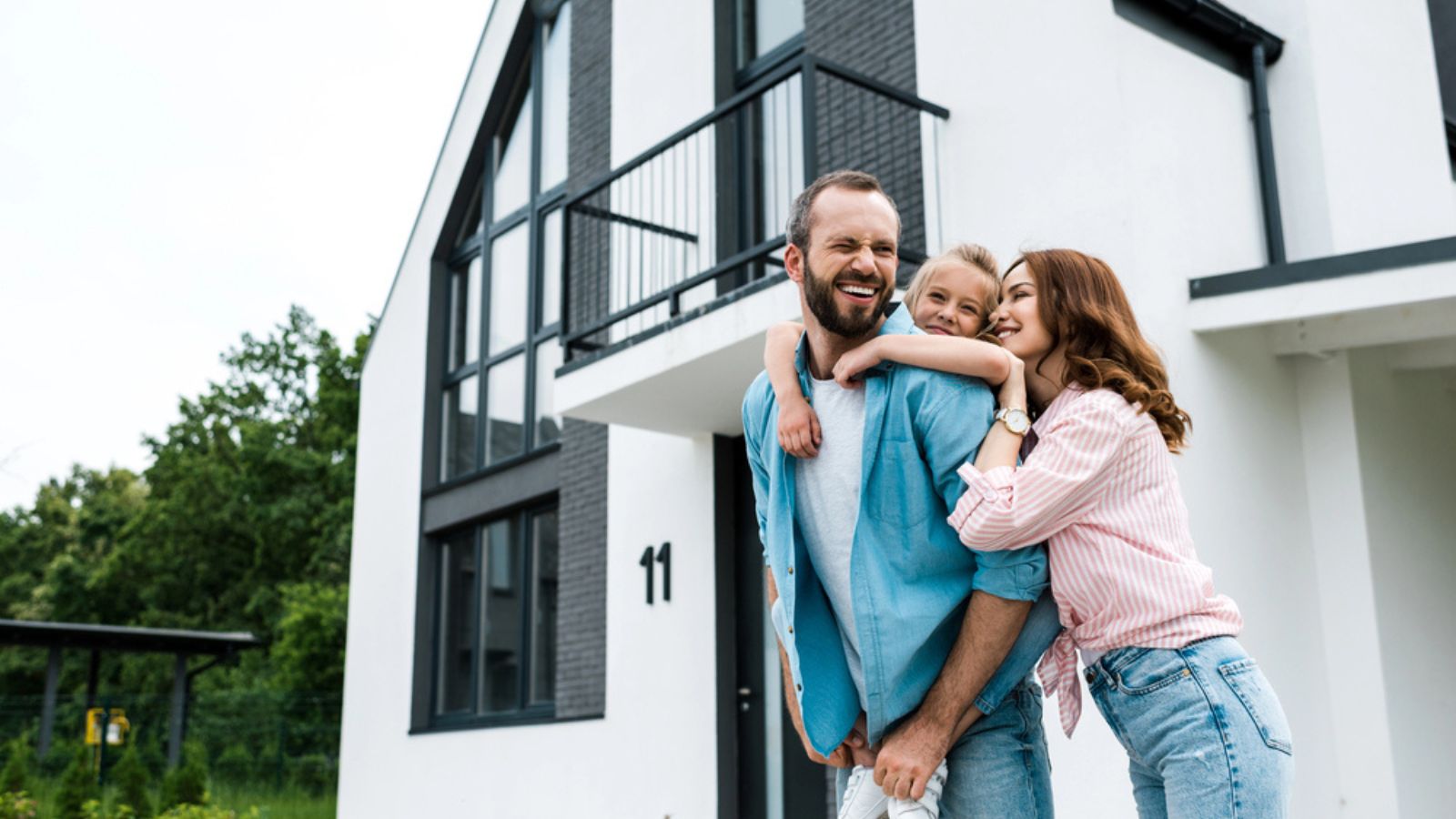 Happy bearded man piggybacking daughter near cheerful wife and home. Property