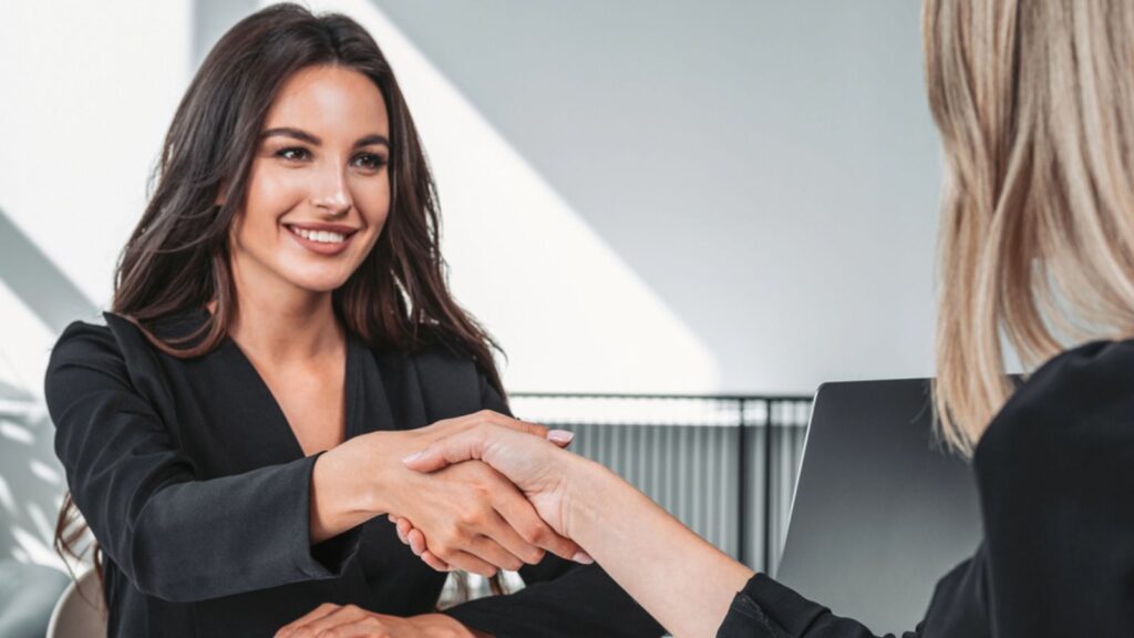Businesswoman in black suit smiling, office room with desk and laptop. Profitable business partnership shaking hands. Concept of financial deal and agreement. Work Concept.