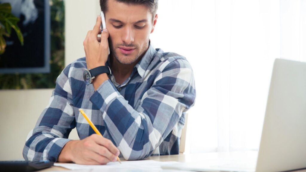 Portrait of a man making notes while on the bills while talking on the phone . Money Concept.