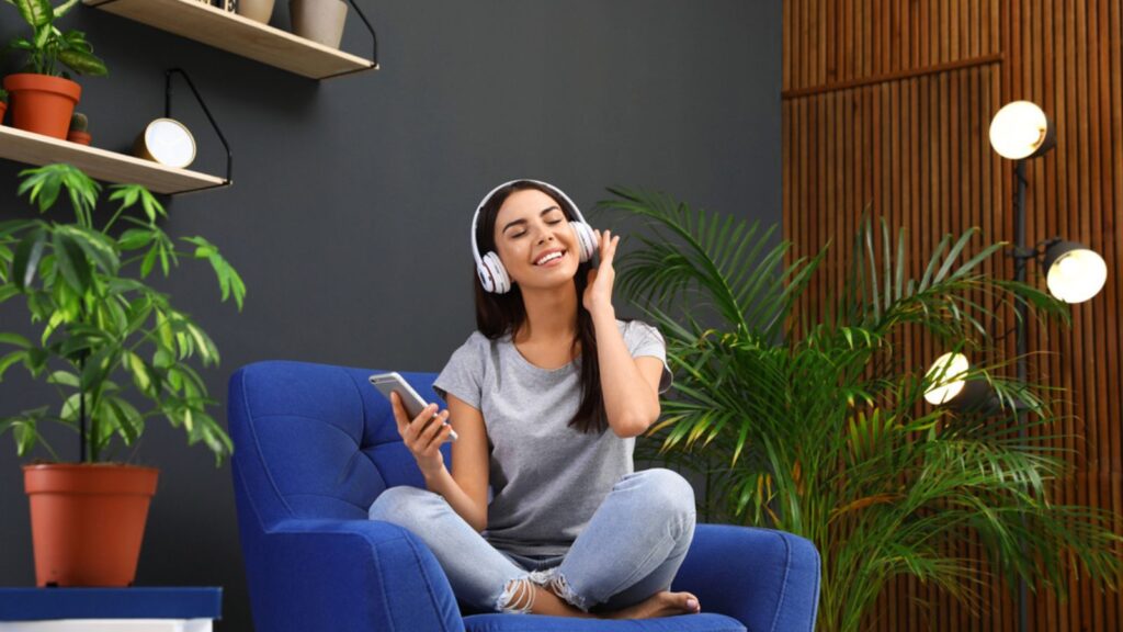 Happy woman listening to music in armchair at home. Indoor plants for trendy interior design