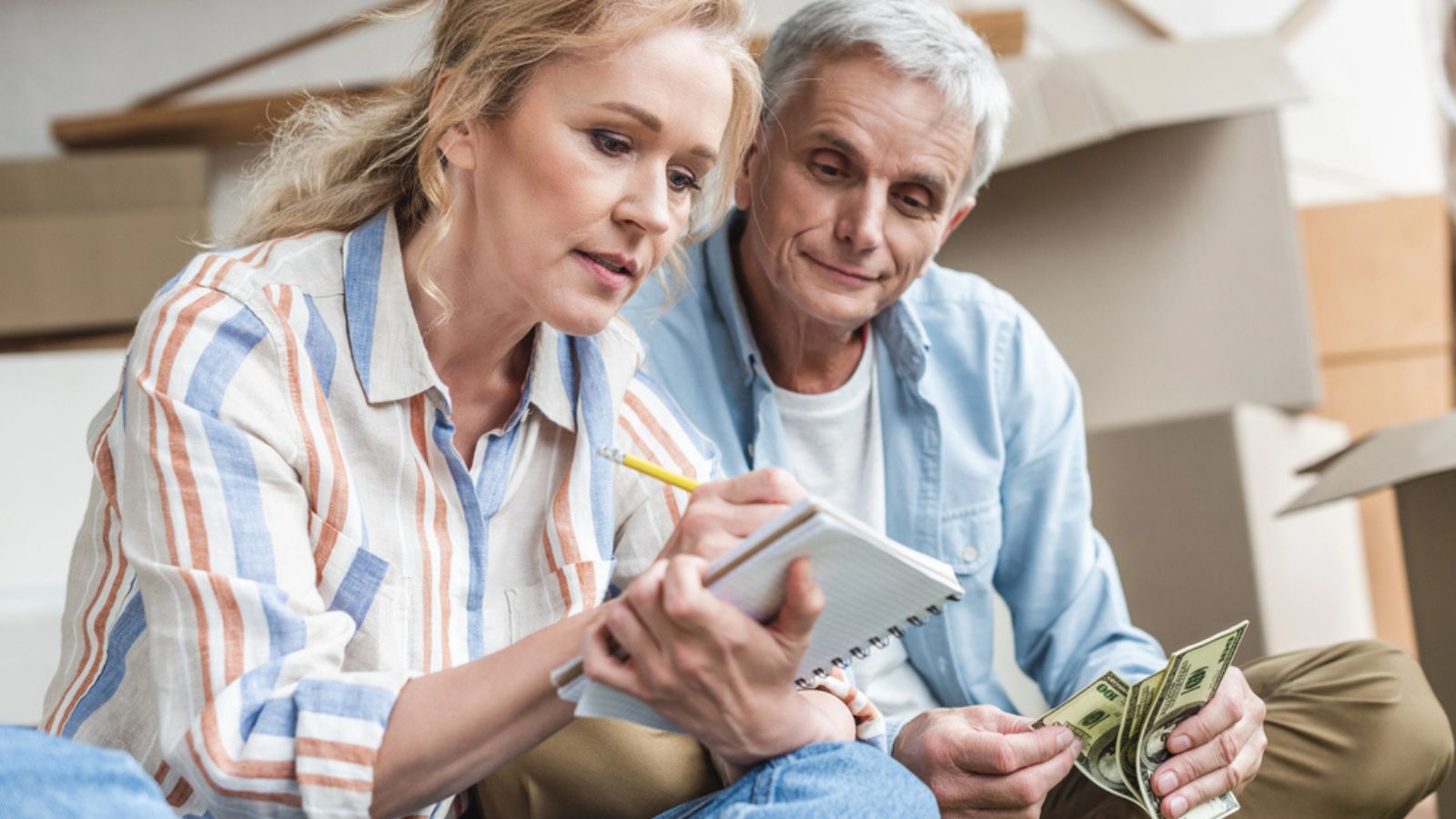 Focused senior couple taking notes and counting money while moving home