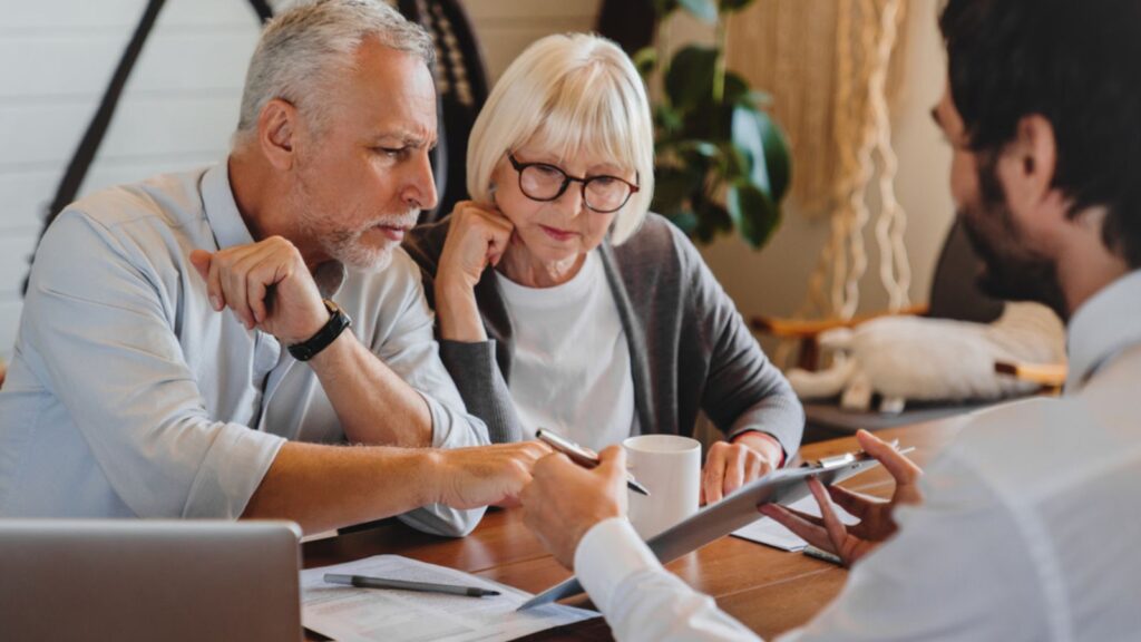 Financial advisor explaining paperwork to elderly retired couple front of desk