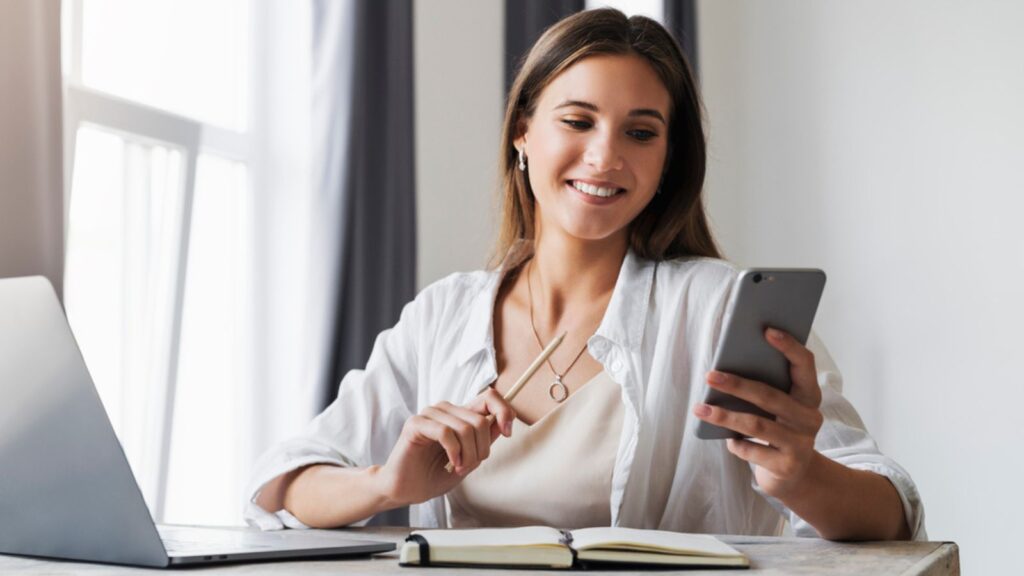 Attractive business woman sits at table in front of laptop and talks on mobile phone, negotiates on the phone