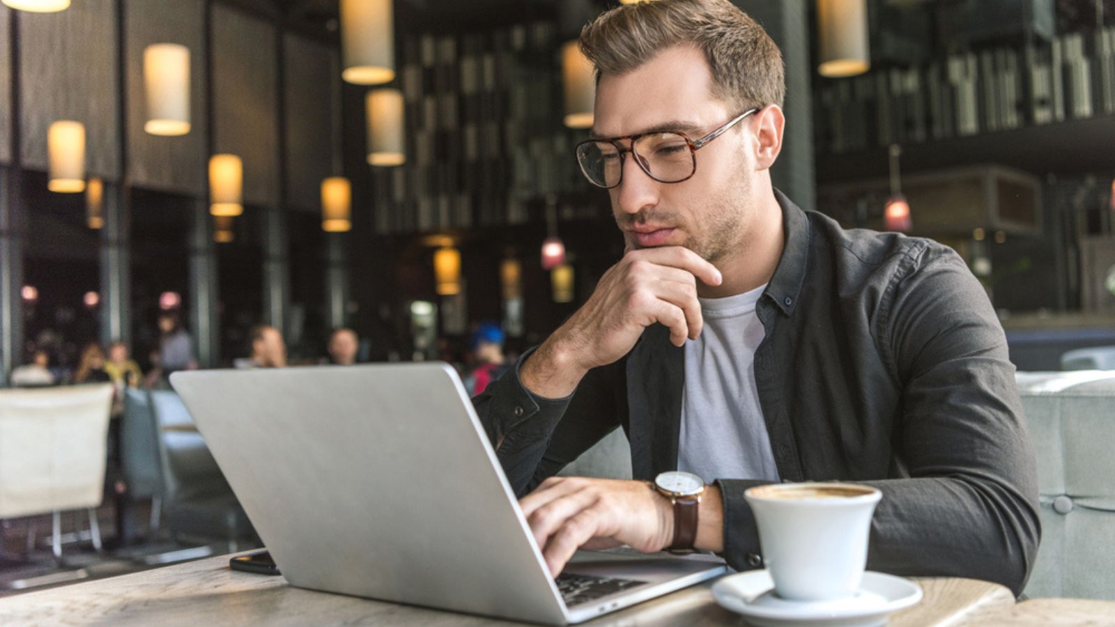 Handsome young freelancer working with laptop in cafe with cup of coffee on table