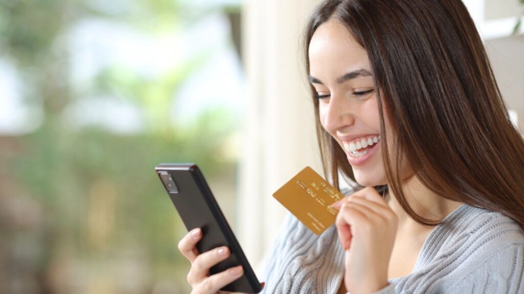 Happy woman buying online with credit card and phone in a house interior