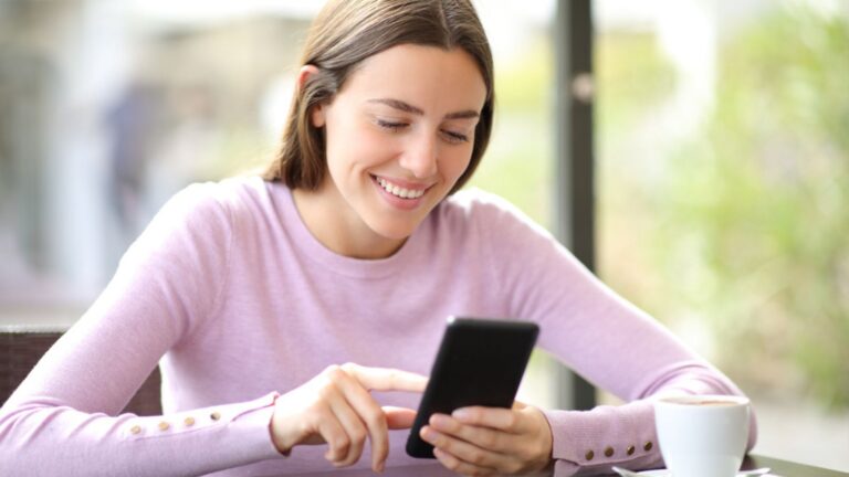 Happy woman using mobile phone checking online content sitting in a coffee shop