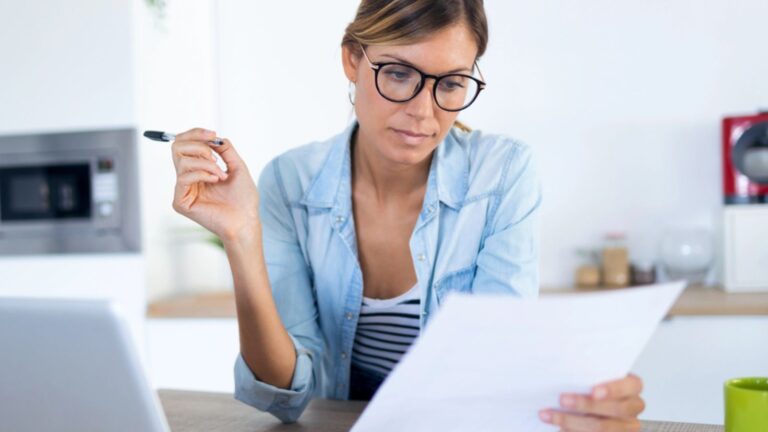 Pretty young woman working with laptop and documents in the kitchen