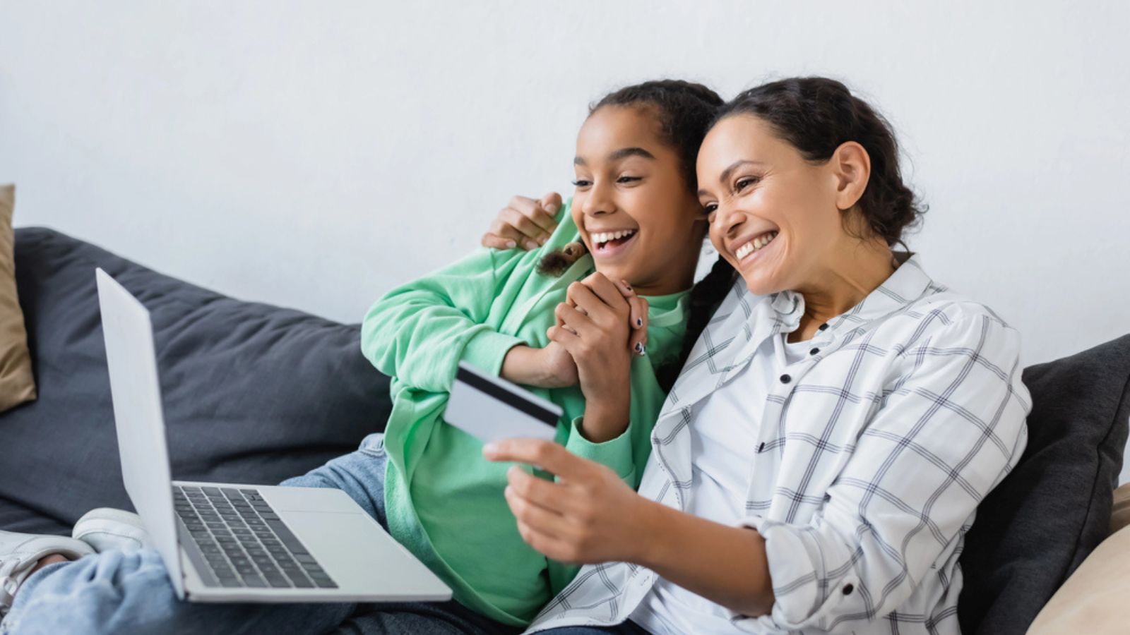 Smiling african american woman holding credit card near laptop and excited daughter