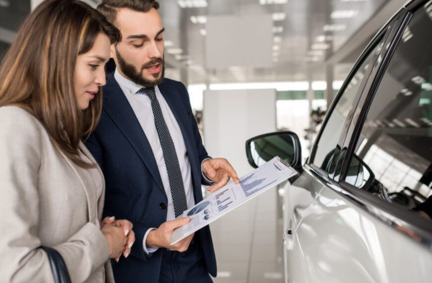 Side view portrait of modern young woman listening to car dealer while choosing luxury car in showroom
